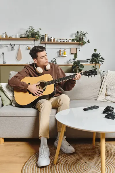 A young man plays guitar on a comfy sofa in a homely living room filled with plants and decor. — Stock Photo