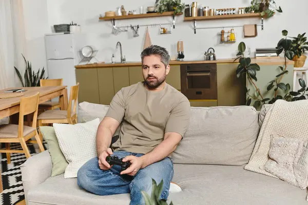 Un hombre se relaja en un sofá suave mientras juega, rodeado de un elegante y acogedor interior de la casa. - foto de stock