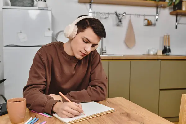 A young man enjoys a cozy evening at home, writing creatively while listening to calming music. — Stock Photo