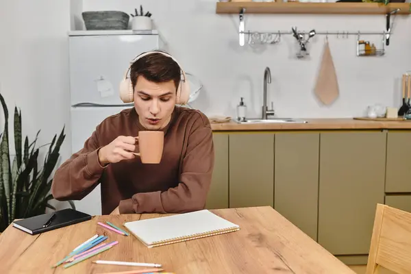 Sipping a warm drink, a man sits at a table, ready for a creative afternoon at home. — Stock Photo