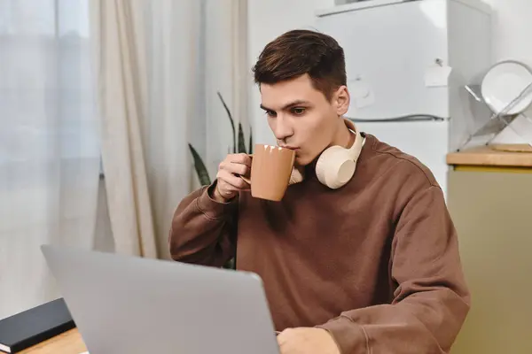 A young man sips coffee while focused on his laptop in a comfortable home environment. — Stock Photo