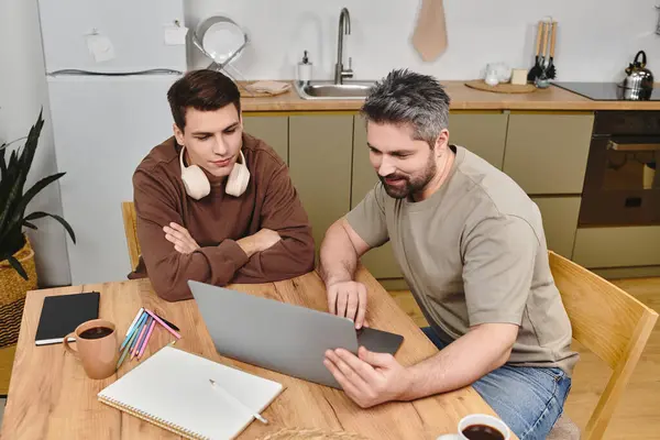 Two brothers sit together at a wooden table, engaged in a collaborative activity with a laptop. — Stock Photo