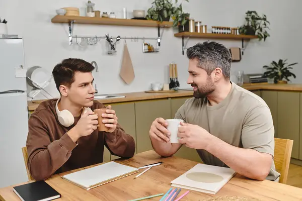 Two brothers enjoy their morning drinks at a cozy kitchen table, sharing smiles and laughter. — Stock Photo
