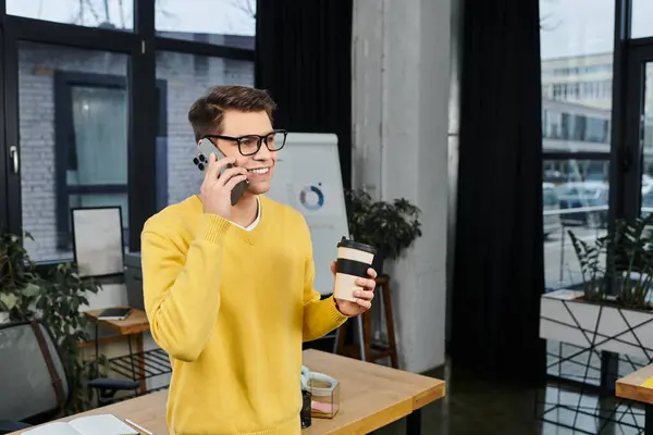 A young professional happily talks on the phone while sipping coffee on their first day at work. — Stock Photo