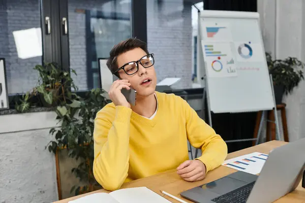A young professional in a yellow sweater engages on a call while seated at an office desk. — Stock Photo