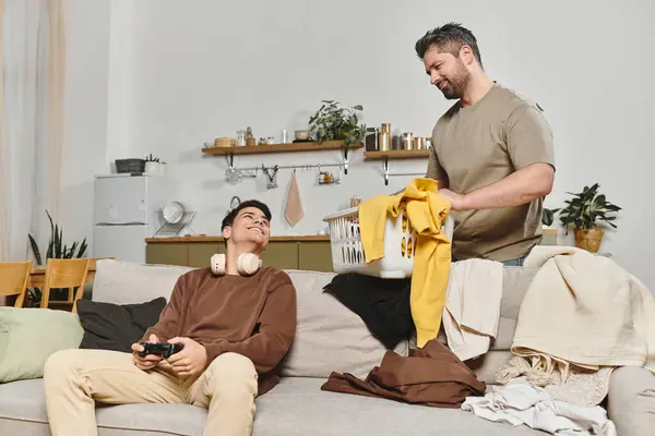 Ein Mann hilft beim Aufräumen, während ein jüngerer Mann in gemütlicher Wohnzimmeratmosphäre spielt. — Stockfoto