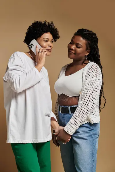 Two fashionable women enjoy a tender moment while talking on the phone, radiating joy. — Stock Photo