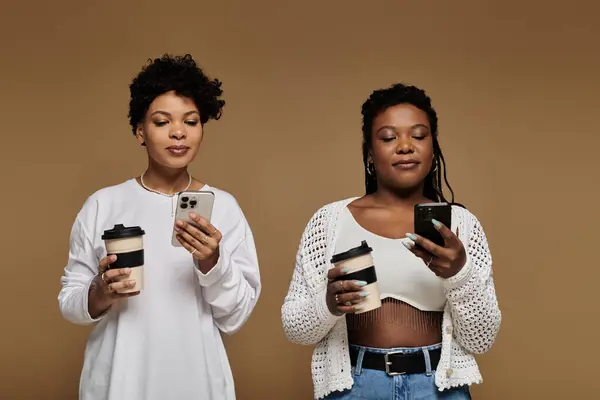 Dos mujeres de moda comparten un momento con café y teléfonos inteligentes en un ambiente vibrante. - foto de stock