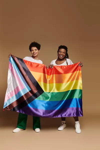 Two stylish women proudly hold a rainbow flag, showcasing their love in a bright setting. — Stock Photo
