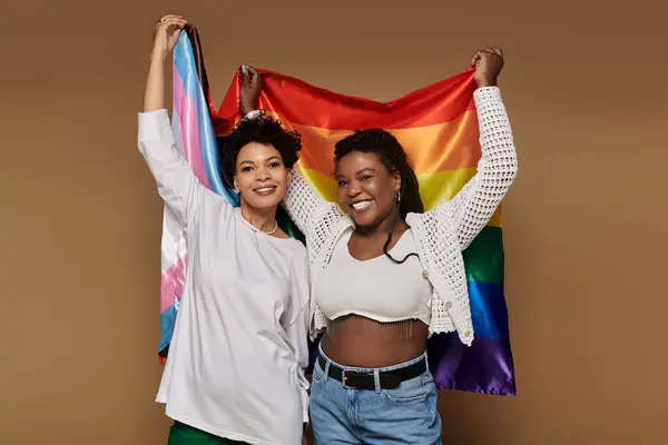 Two fashionable women proudly display rainbow and transgender flags, radiating joy and love. — Stock Photo
