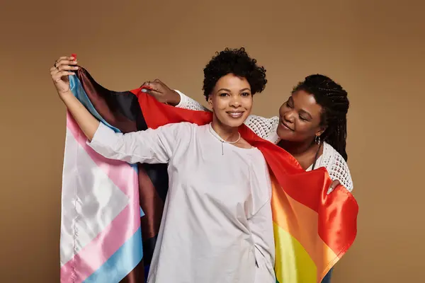 Duas mulheres bonitas compartilham um momento alegre, envoltas em bandeiras coloridas de orgulho, irradiando amor e estilo. — Fotografia de Stock