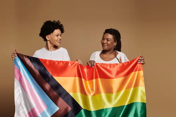 Two joyful women proudly display a colorful pride flag while radiating love and style. — Stock Photo