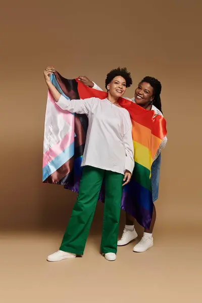 Two stylish women cheerfully wave colorful pride flags to support the LGBT community. — Stock Photo
