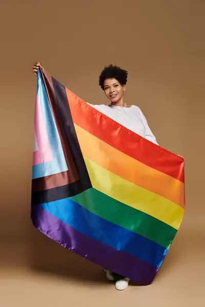 Woman joyfully displays a colorful rainbow flag, celebrating love and pride in a chic location. — Stock Photo