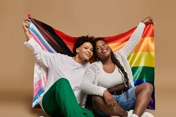 Two stylish women joyfully embrace, celebrating love among colorful flags in a chic setting. — Stock Photo