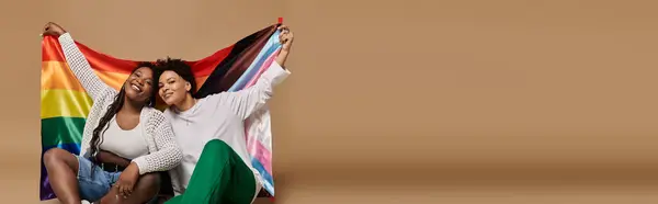 A lovely lesbian couple proudly displays a pride flag, radiating love in stylish outfits. — Stock Photo