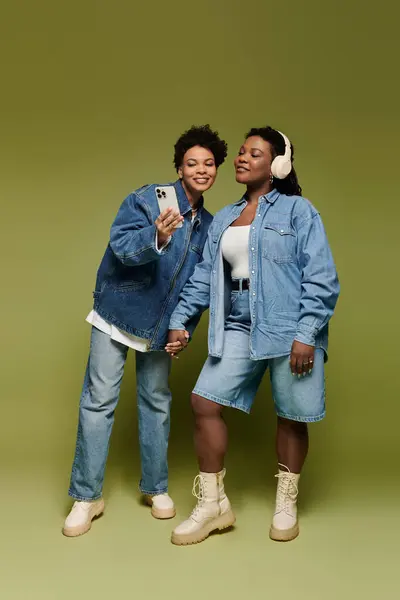 Two fashionable women hold hands and smile while taking a selfie in their trendy outfits. — Stock Photo