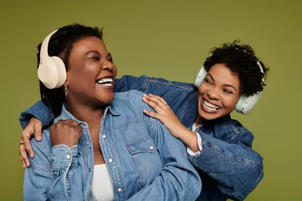 Two stylish women enjoy a lively moment together while wearing trendy headphones and denim outfits. — Stock Photo