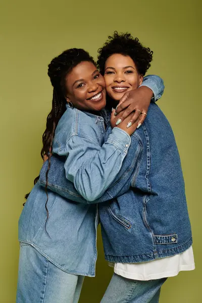 Two stylish women embrace, flaunting their denim against a vibrant backdrop. — Stock Photo
