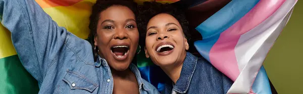 Two joyful women embrace their love under colorful flags, radiating style and happiness together. — Stock Photo