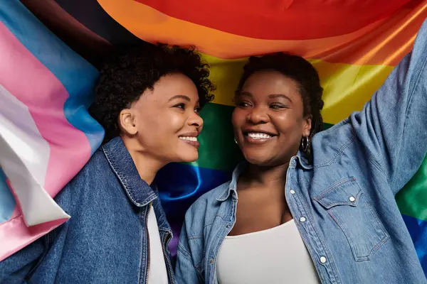 Duas mulheres elegantes compartilham um momento alegre juntas sob uma exibição vibrante de bandeiras de orgulho. — Fotografia de Stock