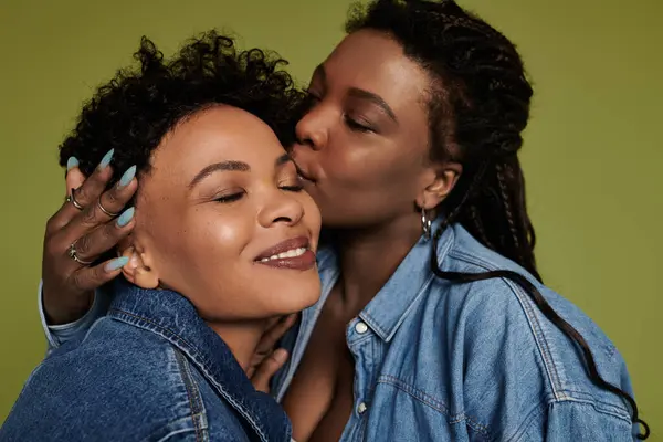 Two stylish women share a tender kiss, radiating love and happiness in a vibrant setting. — Stock Photo