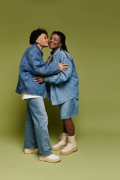 Two stylish women share a tender kiss, expressing their love and fashion sense in matching denim. — Stock Photo
