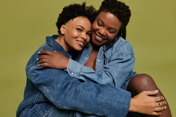A loving lesbian couple embraces each other in stylish denim attire against a vivid backdrop. — Stock Photo