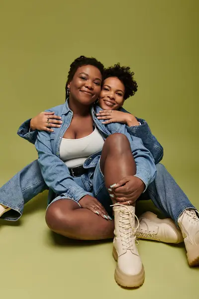 Two stylish women embrace joyfully in chic denim against a vibrant green backdrop. — Stock Photo