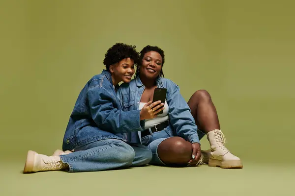 Two fashionable women share a joyful moment while looking at a phone, radiating love and style. — Stock Photo