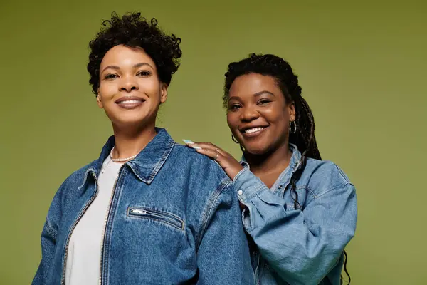 Two stylish women enjoy a playful moment in vibrant outfits against a bright green backdrop. — Stock Photo
