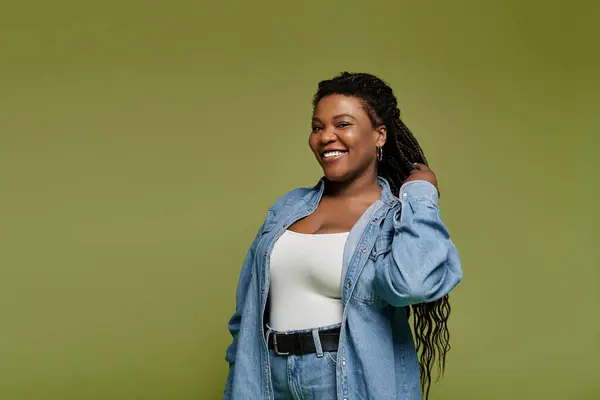 Delighted african american woman in vibrant denim attire with long hair posing on olive backdrop. — Stock Photo