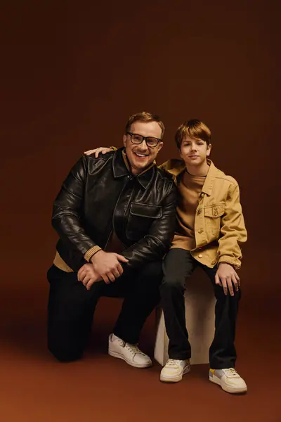 A happy father crouches beside his son, both dressed casually, showcasing their bond in a studio. — Stock Photo