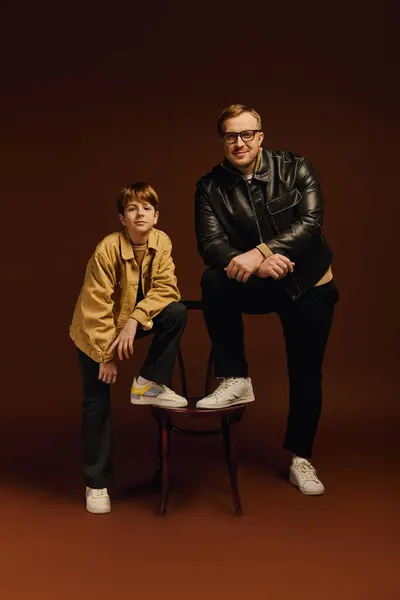 A father and son share a joyful moment, showcasing casual outfits in a cozy studio setting. — Stock Photo