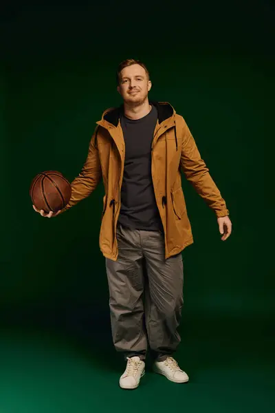 A good looking man stands confidently in a studio, casually dressed and holding a basketball. — Stock Photo