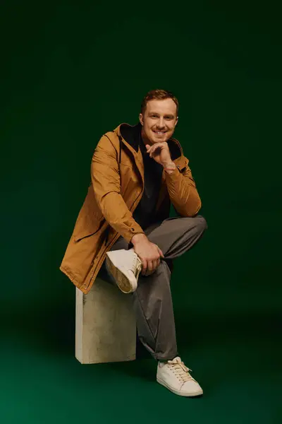 Confidently seated, a handsome man showcases his casual style in a vibrant studio environment. — Stock Photo