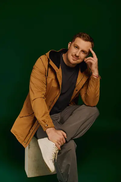 A handsome man in a casual outfit sits thoughtfully on a block, highlighting modern fashion. — Stock Photo