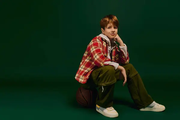 Un garçon préadolescent élégant pose avec confiance dans des vêtements décontractés dans un riche fond vert. — Photo de stock