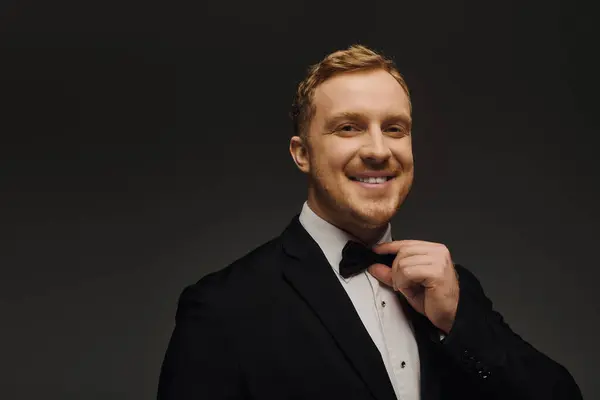 Handsome man dressed in a tuxedo adjusts his bow tie while posing confidently in a studio. — Stock Photo