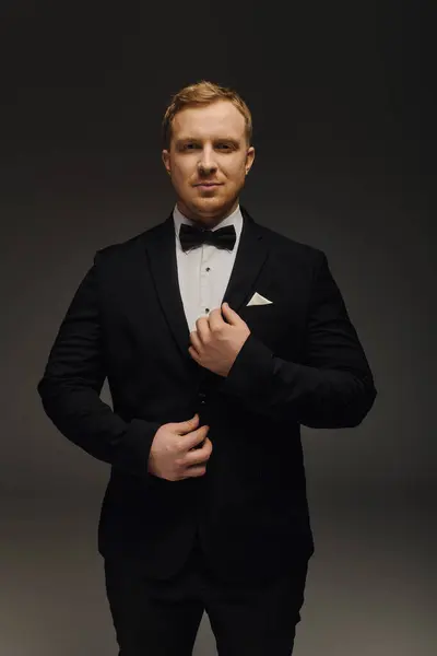 A dapper man stands confidently in an elegant tuxedo with a bow tie, exuding charm. — Stock Photo