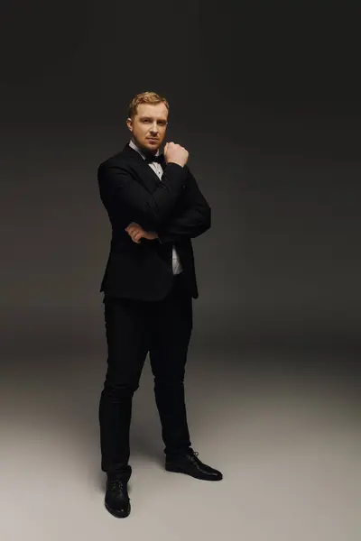 A handsome man stands poised in a stylish tuxedo, showcasing elegance and charm in a sleek studio. — Stock Photo