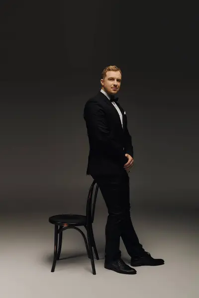 A handsome man stands poised in a tuxedo, showcasing classic fashion and confidence in a studio. — Stock Photo