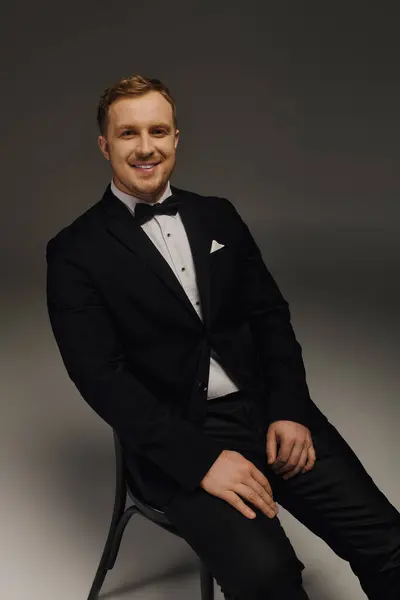 Ein fescher Mann sitzt selbstbewusst in einem Studio, gekleidet in elegantem Smoking und Fliege. — Stockfoto