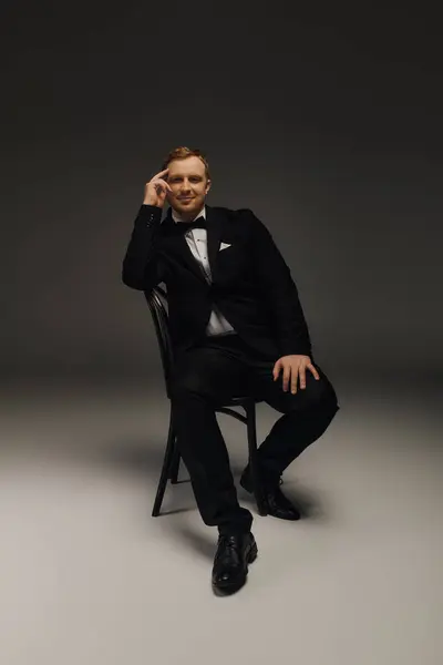A handsome man sits confidently in a studio, dressed impeccably in a tuxedo and bow tie. — Stock Photo