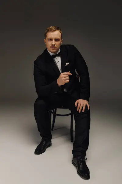 A stylish man in a tuxedo sits confidently on a chair, showcasing his poised demeanor. — Stock Photo