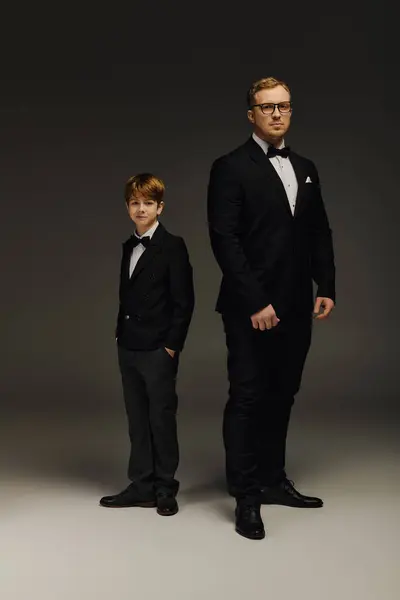 Dressed in matching tuxedos, a handsome father and son pose elegantly in a modern studio. — Stock Photo