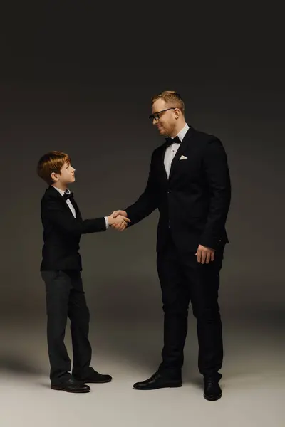 Father and son share a warm handshake in stylish tuxedos, exuding sophistication and charm. — Stock Photo