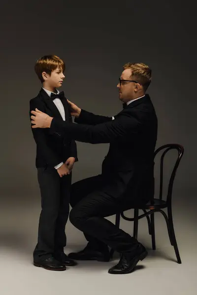 Father adjusts the bow tie of his son in an elegant studio atmosphere, showcasing family love. — Stock Photo