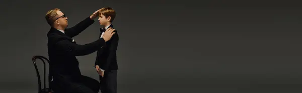 Dressed in matching tuxedos, a father and son enjoy a bonding moment in an upscale studio, banner — Stock Photo