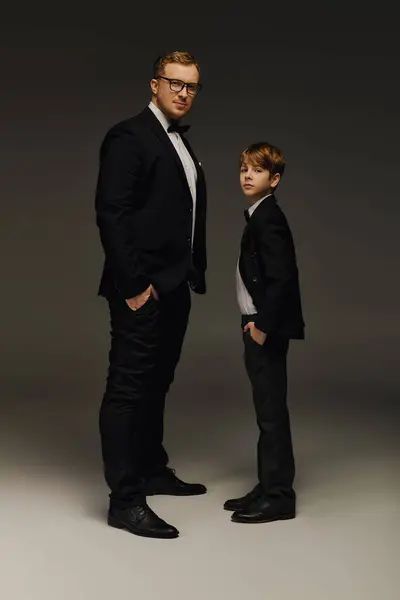 Father and son stand confidently in tuxedos with bow ties in a studio. — Stock Photo